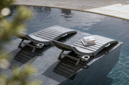 Two lounge chairs by a pool with a book on one of them.