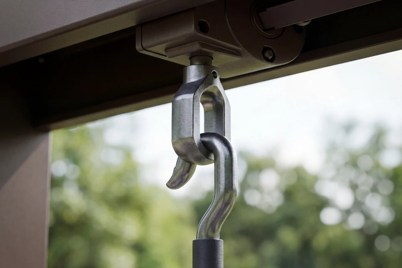 Close-up of a metal hook attached to an overhead structure with a blurred natural background