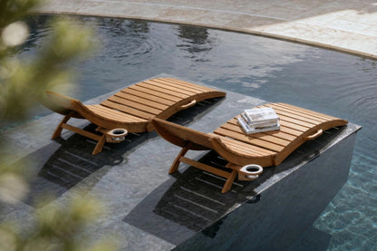 Two wooden lounge chairs by a poolside with a towel and reading material.