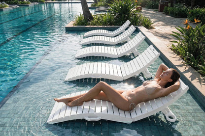 Woman lying on a white lounge chair by a pool with greenery around