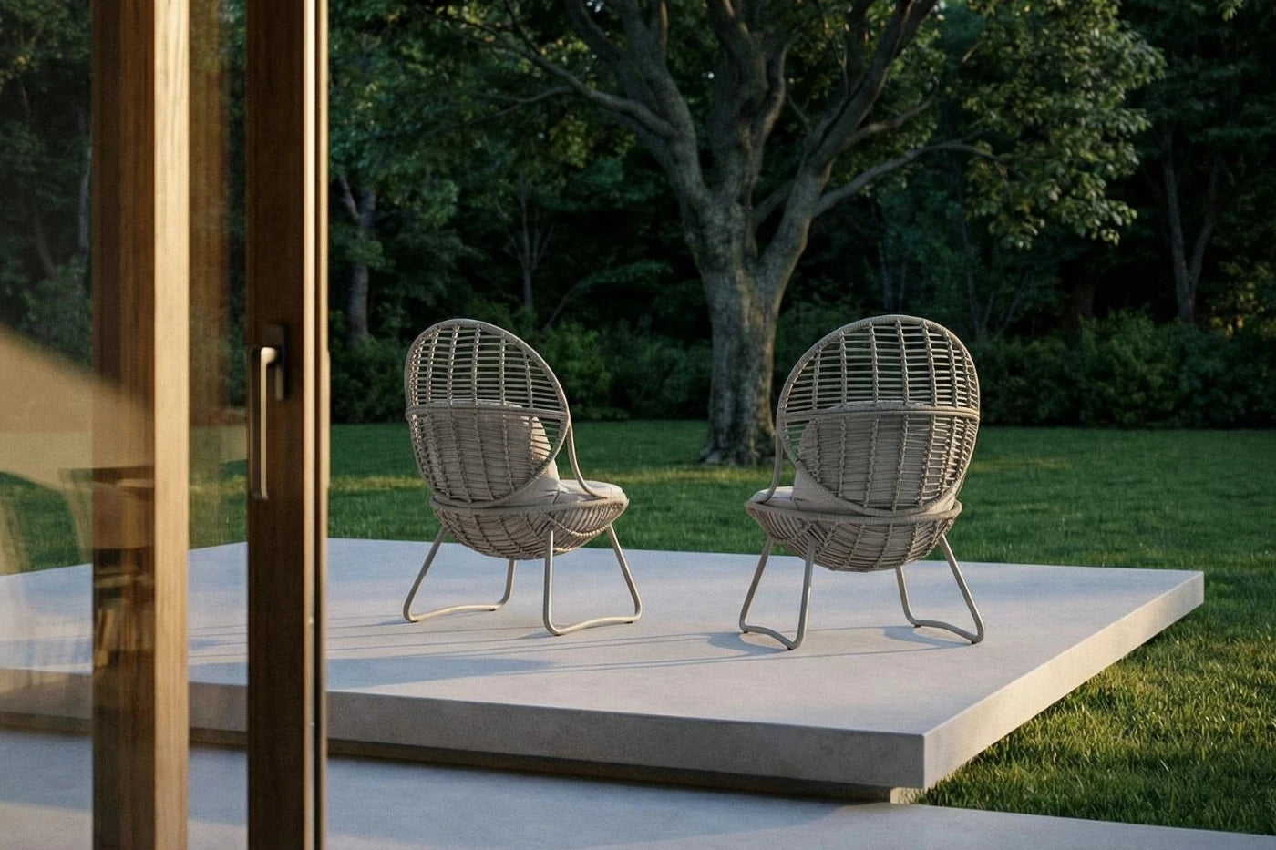 Two wicker chairs on a patio with a garden background