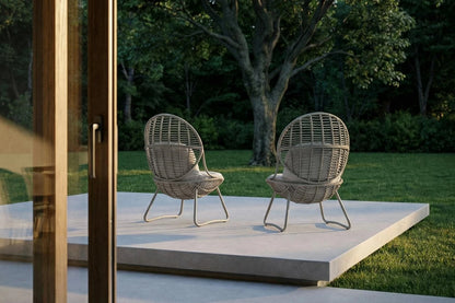 Two wicker chairs on a patio with a garden background