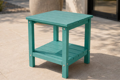 A teal green outdoor side table with a slatted top and lower shelf, shown on a light stone patio.