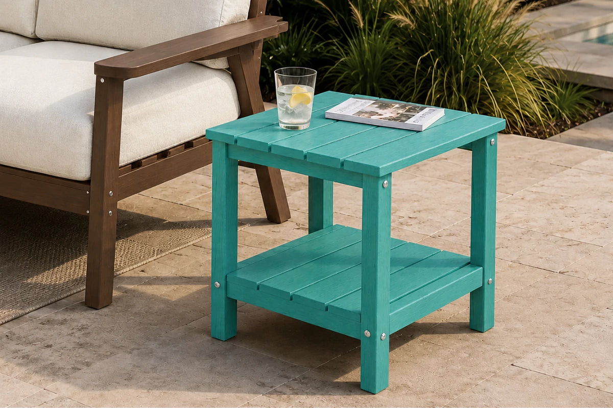 A turquoise outdoor side table with two shelves, shown next to a patio chair on a stone patio. A glass of water and a magazine rest on the tabletop.