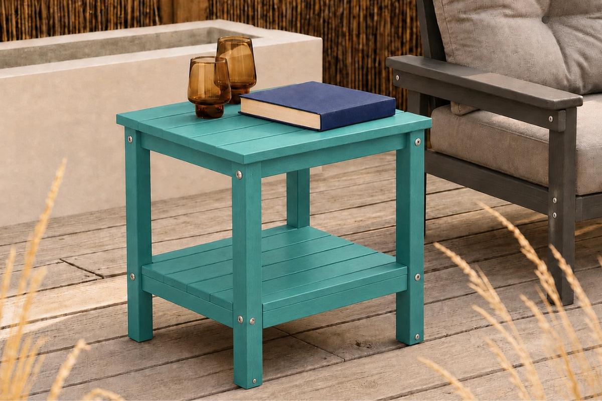 A teal outdoor side table with two shelves, styled on a wooden deck next to a gray armchair with a navy book and amber glasses on top.