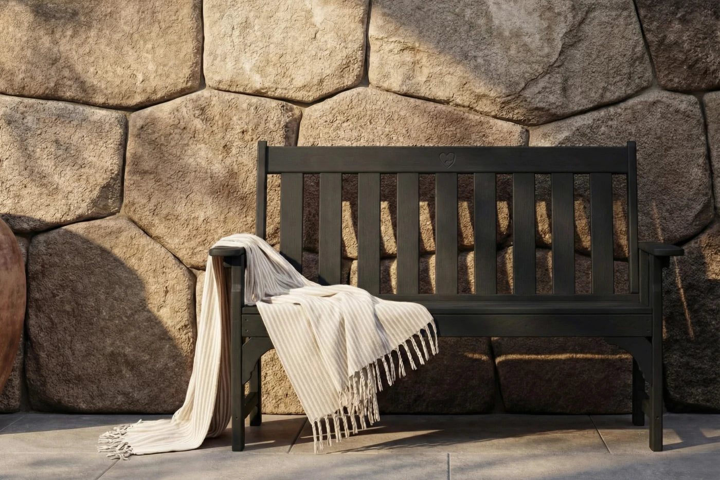 Wooden bench with a blanket draped over it against a stone wall.