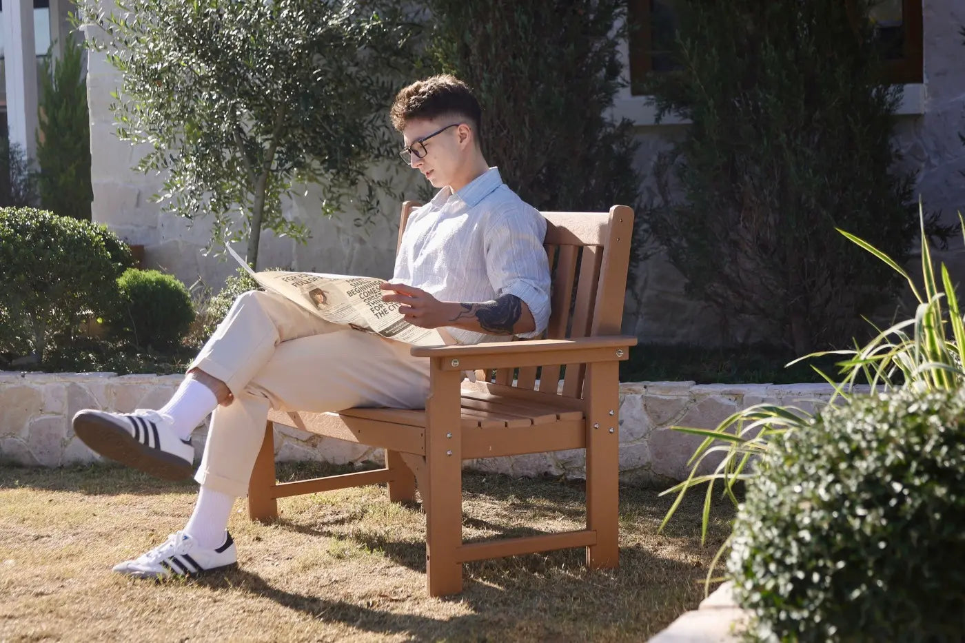 Man sitting on a wooden bench reading a newspaper in a garden.