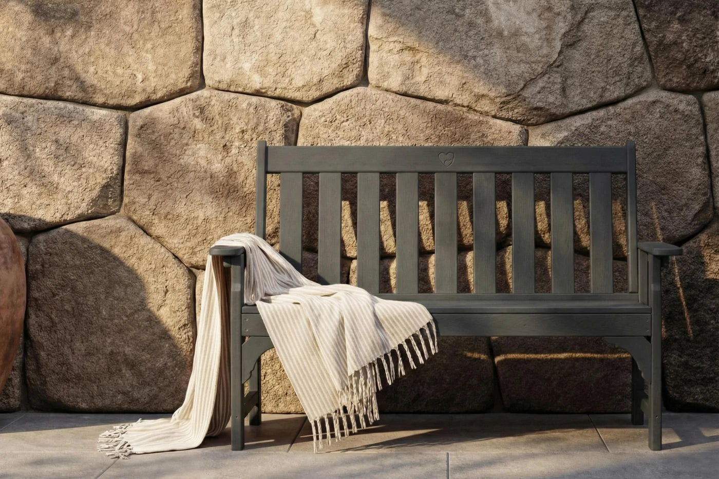 Dark wooden bench with a blanket draped over it against a stone wall.