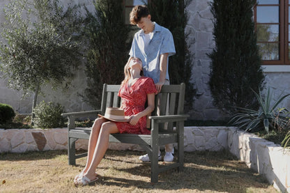 Two people sitting on a bench outdoors with a stone wall and plants in the background.