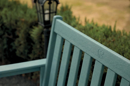 Teal bench with a blurred background of greenery and a lamp post.