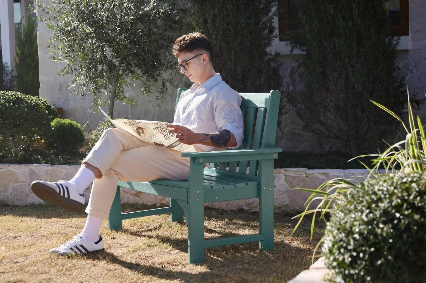 Man reading a newspaper on a green bench outdoors