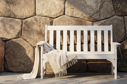 White bench with a blanket draped over it against a stone wall.