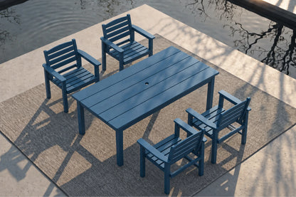 A blue outdoor patio dining set consisting of a rectangular slatted table and four matching armchairs, arranged on a woven rug beside a concrete deck and water.