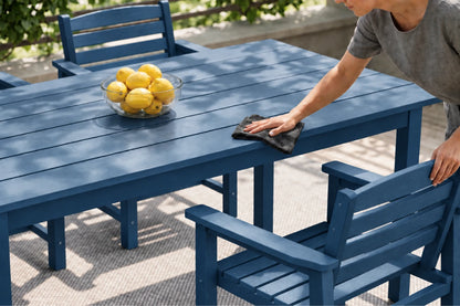 A blue outdoor dining table and matching chairs on a patio, with a person wiping the table surface with a cloth. A glass bowl of lemons sits on the table.