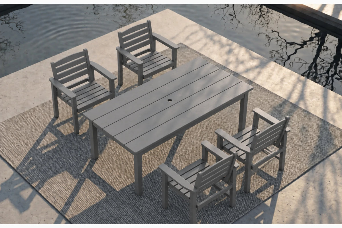 A 5-piece gray outdoor patio dining set consisting of a rectangular slatted table and four matching armchairs, arranged on a textured rug beside a concrete deck and water.