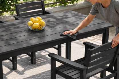 A black outdoor dining table and matching chairs on a patio, with a person wiping the tabletop with a cloth and a bowl of lemons on the table.