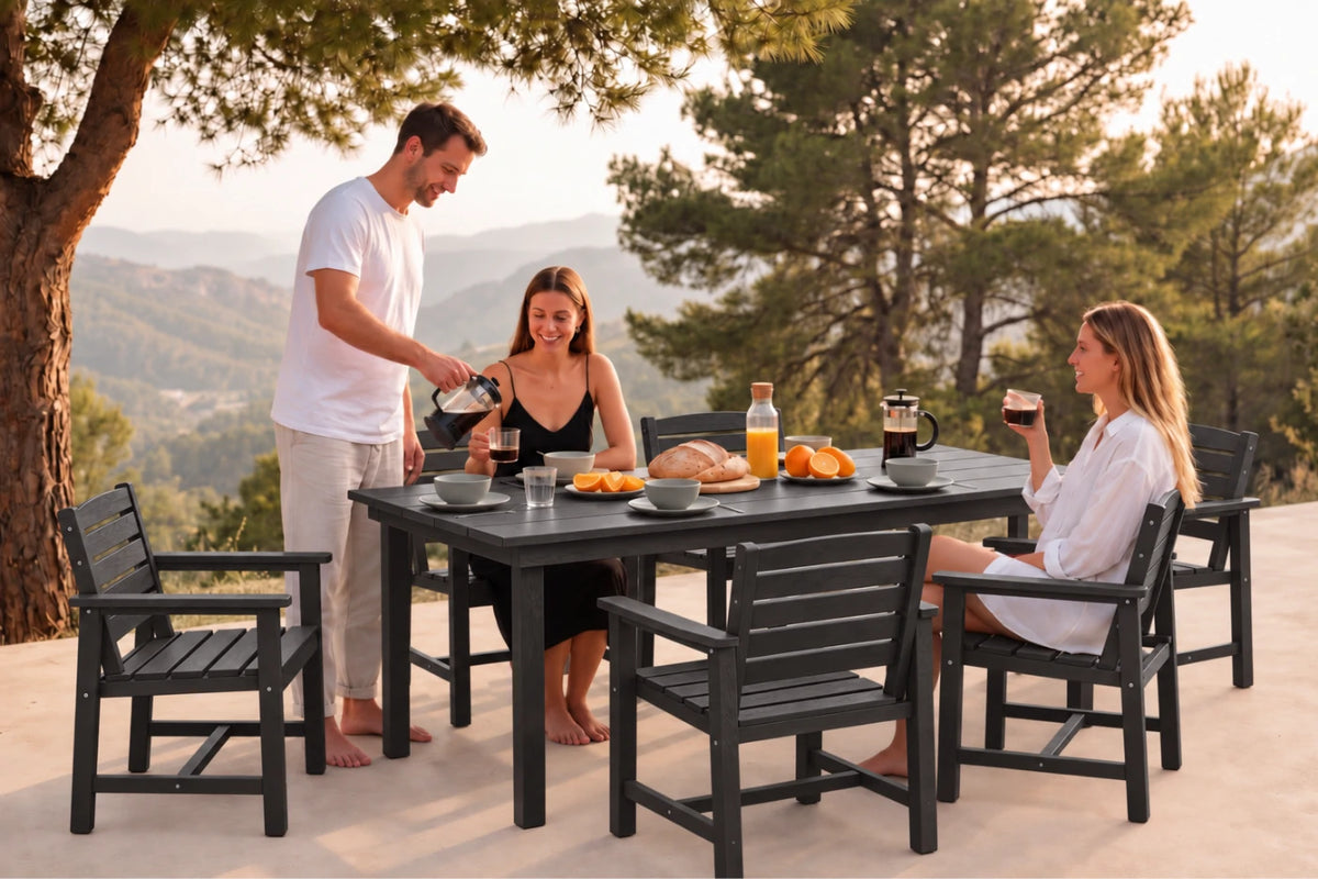 A 7-piece outdoor dining set with a rectangular black table and 6 matching slatted chairs, shown in use with three people having a meal on a patio with a scenic mountain background.