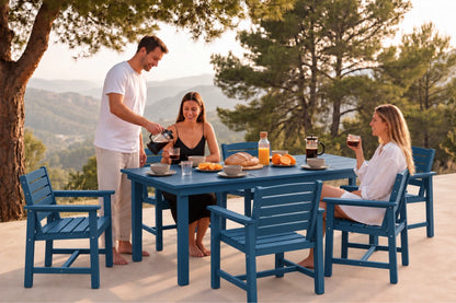 A blue outdoor dining set with a rectangular table and six matching chairs, shown in use by three people having a meal on a patio with trees and a scenic background.