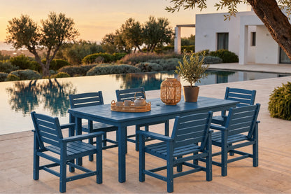 A blue outdoor dining set with a rectangular table and six matching slatted chairs, arranged on a patio beside a swimming pool at sunset. Decorative items on the table include a woven basket and a potted plant.