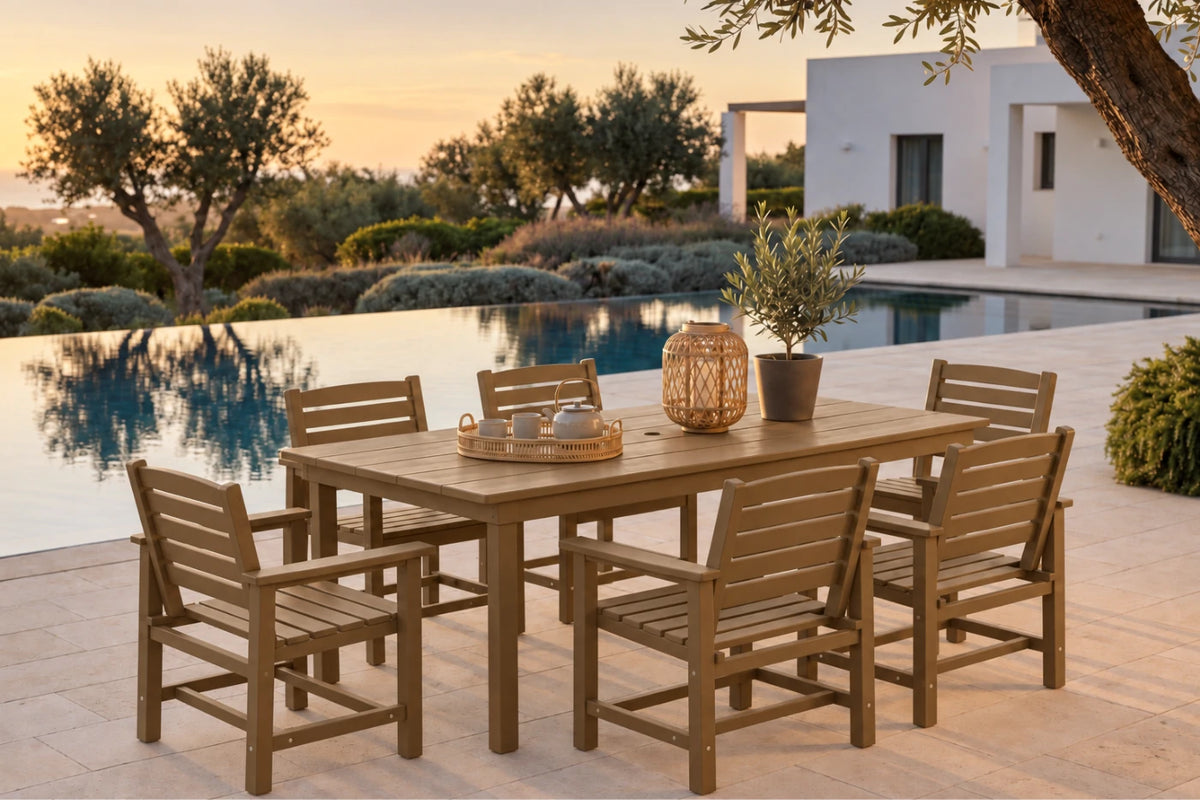 A 7-piece outdoor dining set made of weather-resistant teak wood, featuring a rectangular table and six matching slatted armchairs, styled on a stone patio next to an infinity pool at sunset.
