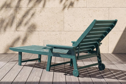 Green lounge chair on a wooden deck with a stone wall background