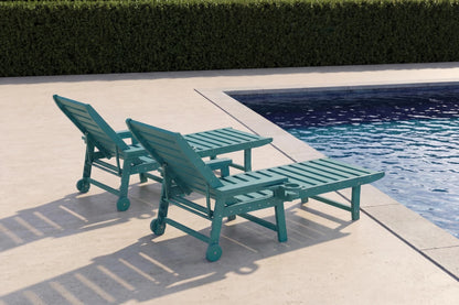 Two teal lounge chairs by a poolside with a hedge in the background