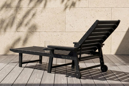 Black outdoor lounge chair on a wooden deck with a stone wall background