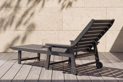 Brown outdoor lounge chair with ottoman on a wooden deck against a beige wall.