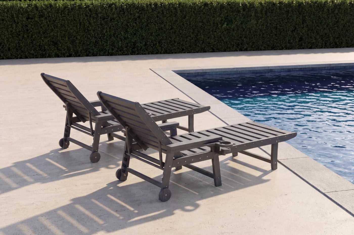 Two dark brown lounge chairs by a pool with a hedge in the background