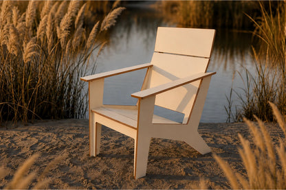 A modern poly Adirondack chair placed on sandy ground beside a calm body of water, with reeds and grasses in the background.
