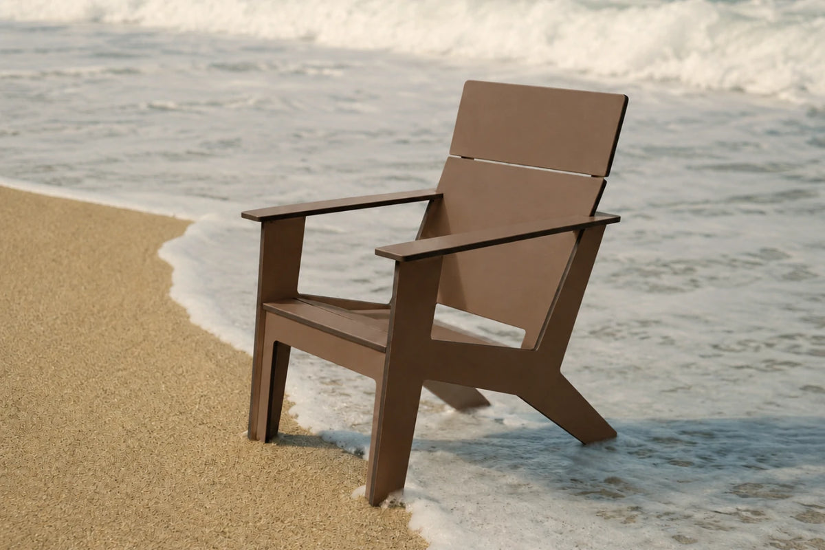 A modern brown outdoor chair positioned on a sandy beach with ocean waves in the background.