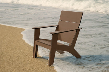 A modern brown outdoor chair positioned on a sandy beach with ocean waves in the background.