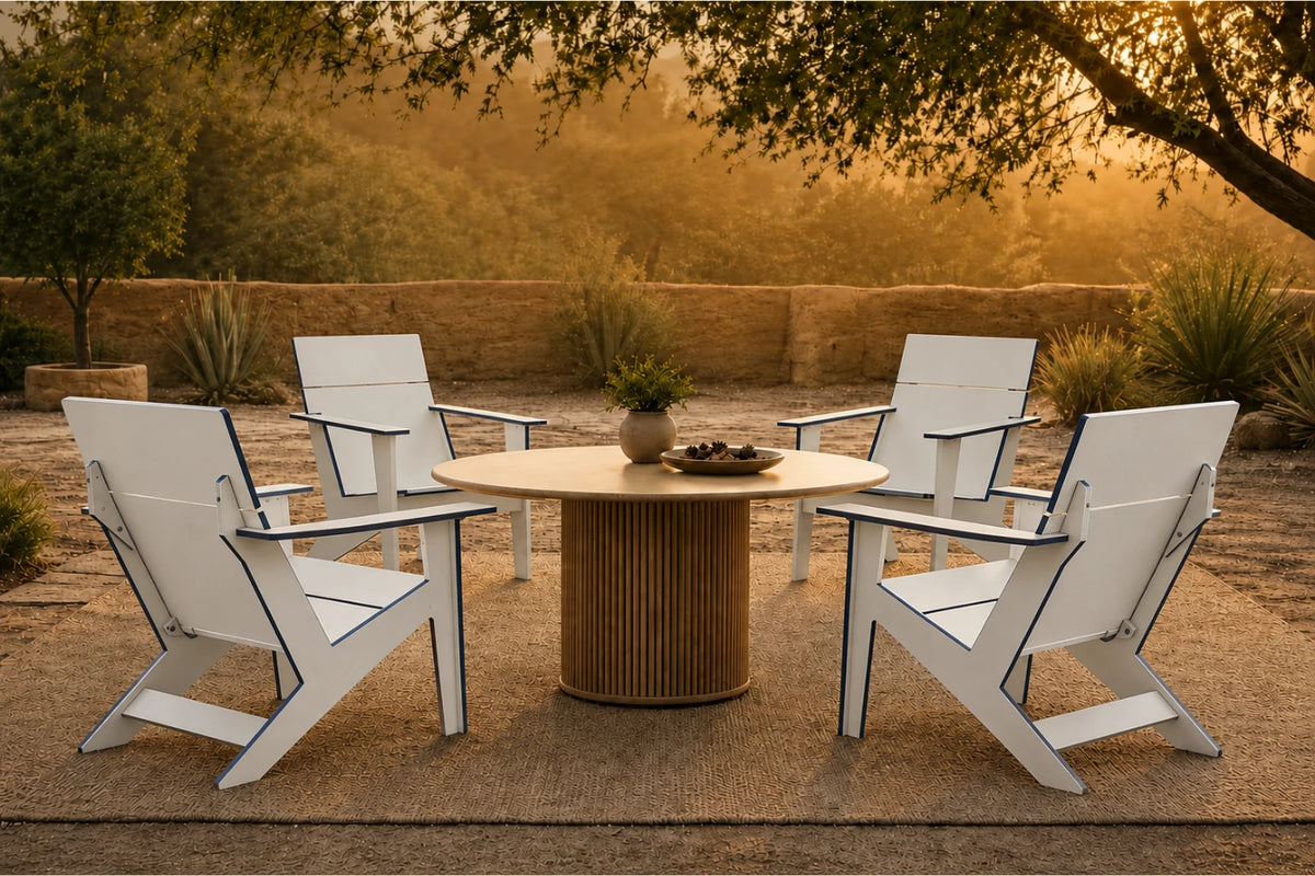 Four white outdoor Adirondack-style chairs arranged around a round slatted wood table on a patio, with trees and warm golden sunlight in the background.