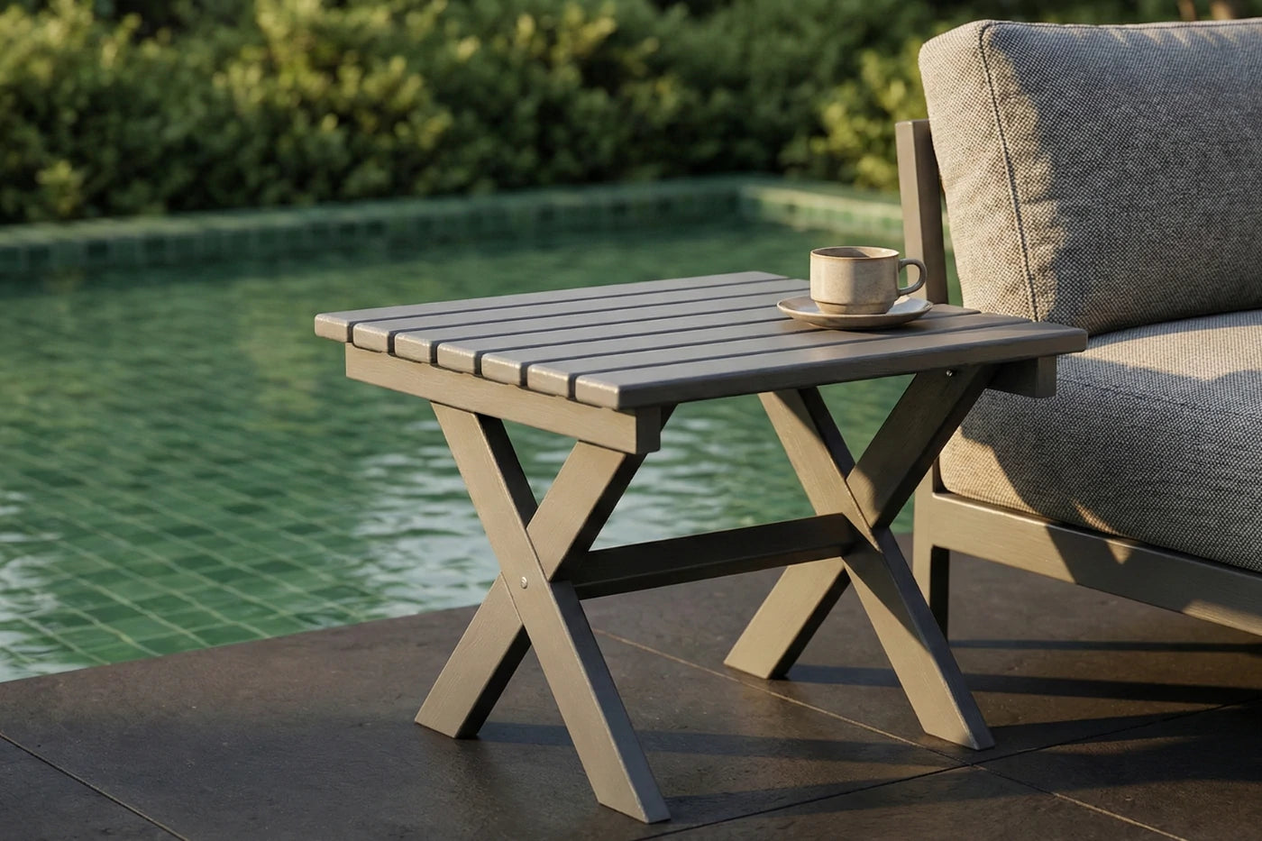 Outdoor table with a cup and saucer next to a couch by a pool