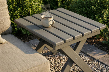 Small outdoor table with a cup of steaming coffee next to a cushioned chair.