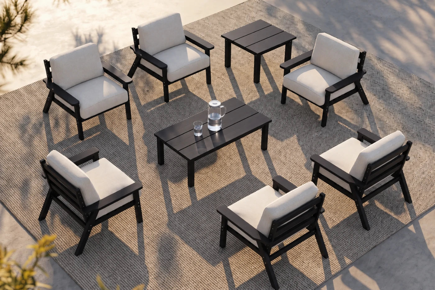 An eight-piece outdoor patio furniture set including six black-framed armchairs with off-white cushions, a rectangular black coffee table, and a matching side table, arranged on a woven rug over a concrete patio.