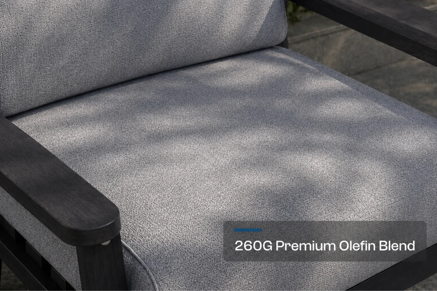 Close-up of a gray textured outdoor chair cushion with a black armrest, featuring a text overlay that reads '260G Premium Olefin Blend'.