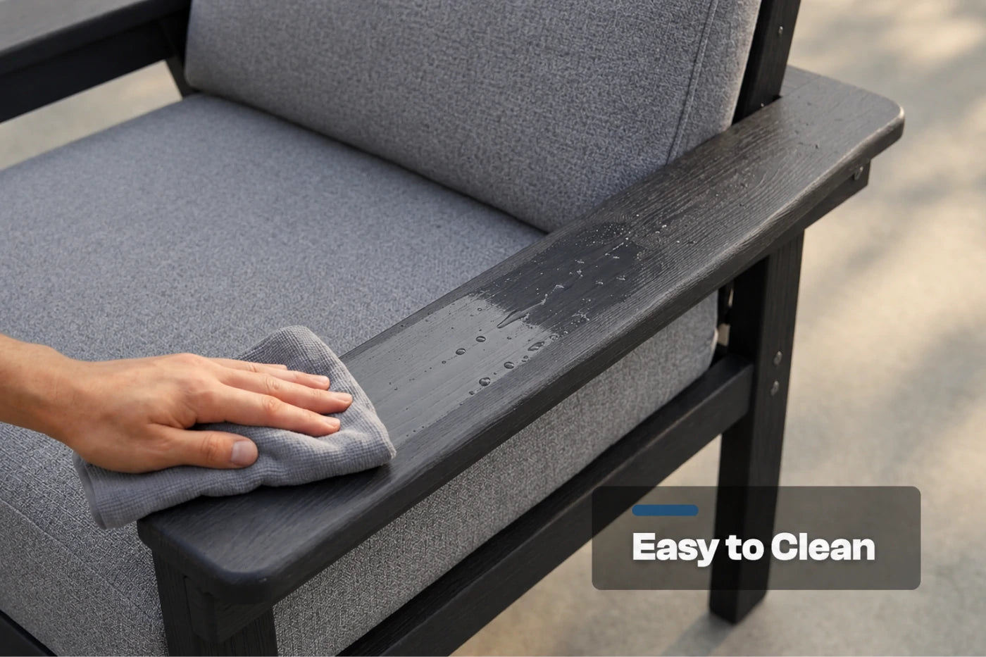 A close-up of a person's hand wiping down the armrest of a gray cushioned outdoor chair with a gray cloth. The chair has a black frame and a text overlay in the bottom right corner that reads 'Easy to Clean'.