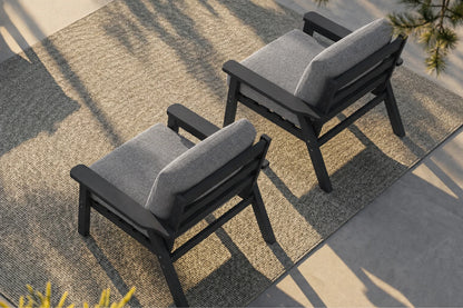 Two outdoor armchairs with black frames and gray cushions, arranged on a textured beige rug in a patio setting with natural shadows.