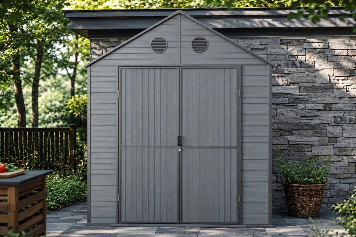 A gray resin storage shed with polycarbonate roof, shown installed against a stone wall in a backyard setting with trees and plants visible.