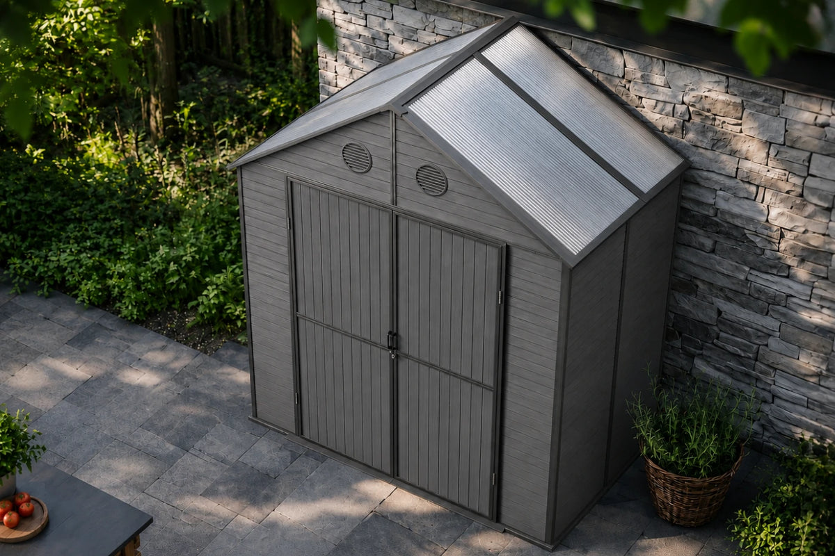 A gray resin storage shed with polycarbonate roof and double doors, shown in a backyard setting next to a stone wall and potted plants.