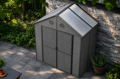 A gray resin storage shed with polycarbonate roof and double doors, shown in a backyard setting next to a stone wall and potted plants.