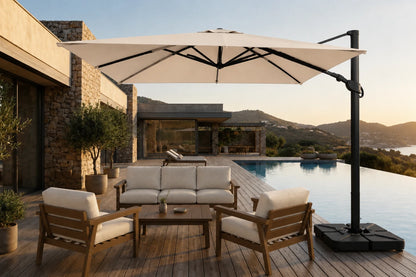 A large beige patio umbrella with a black cantilever pole and weighted base, shading a modern outdoor lounge set with wooden chairs and a sofa on a poolside deck.