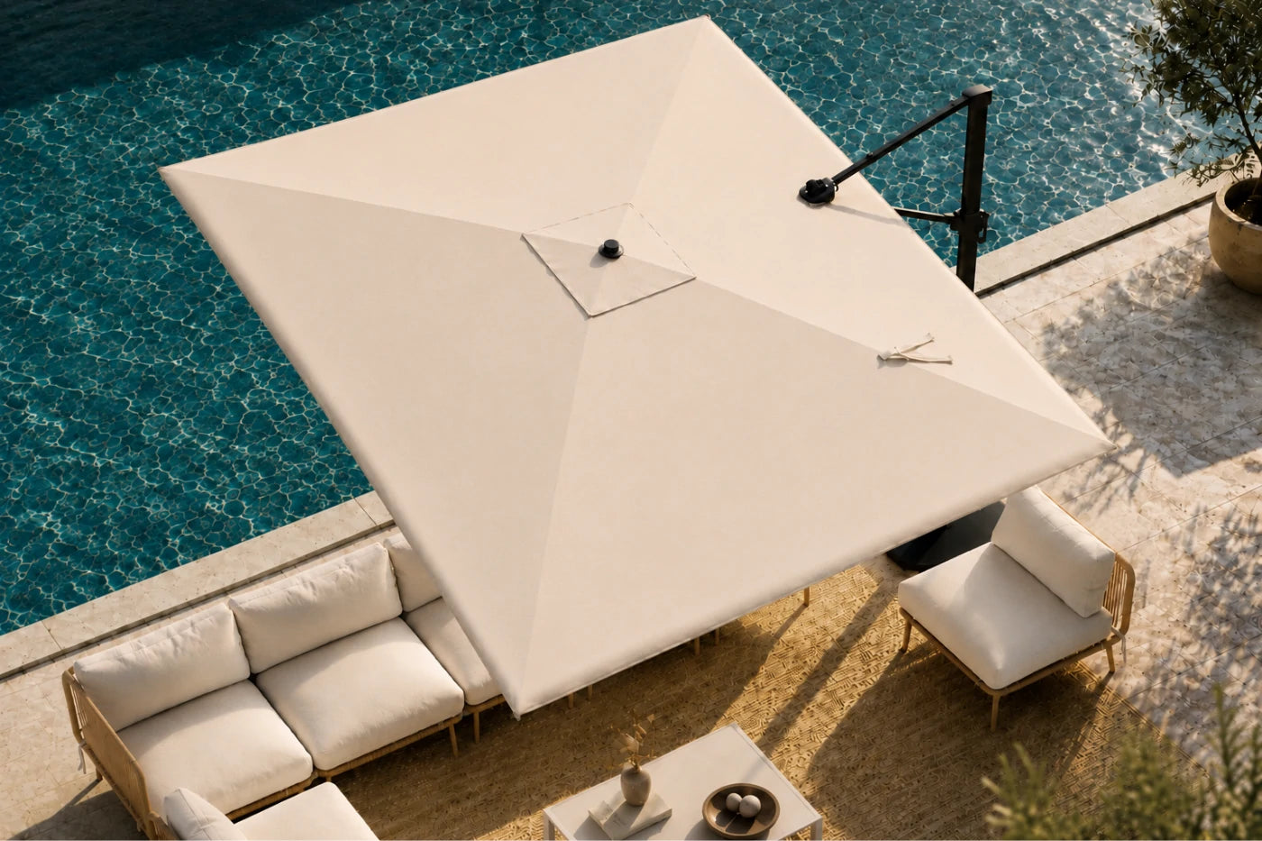 A large patio umbrella in a beige color, shown from an elevated angle next to a swimming pool with a modern outdoor sofa and lounge chair.