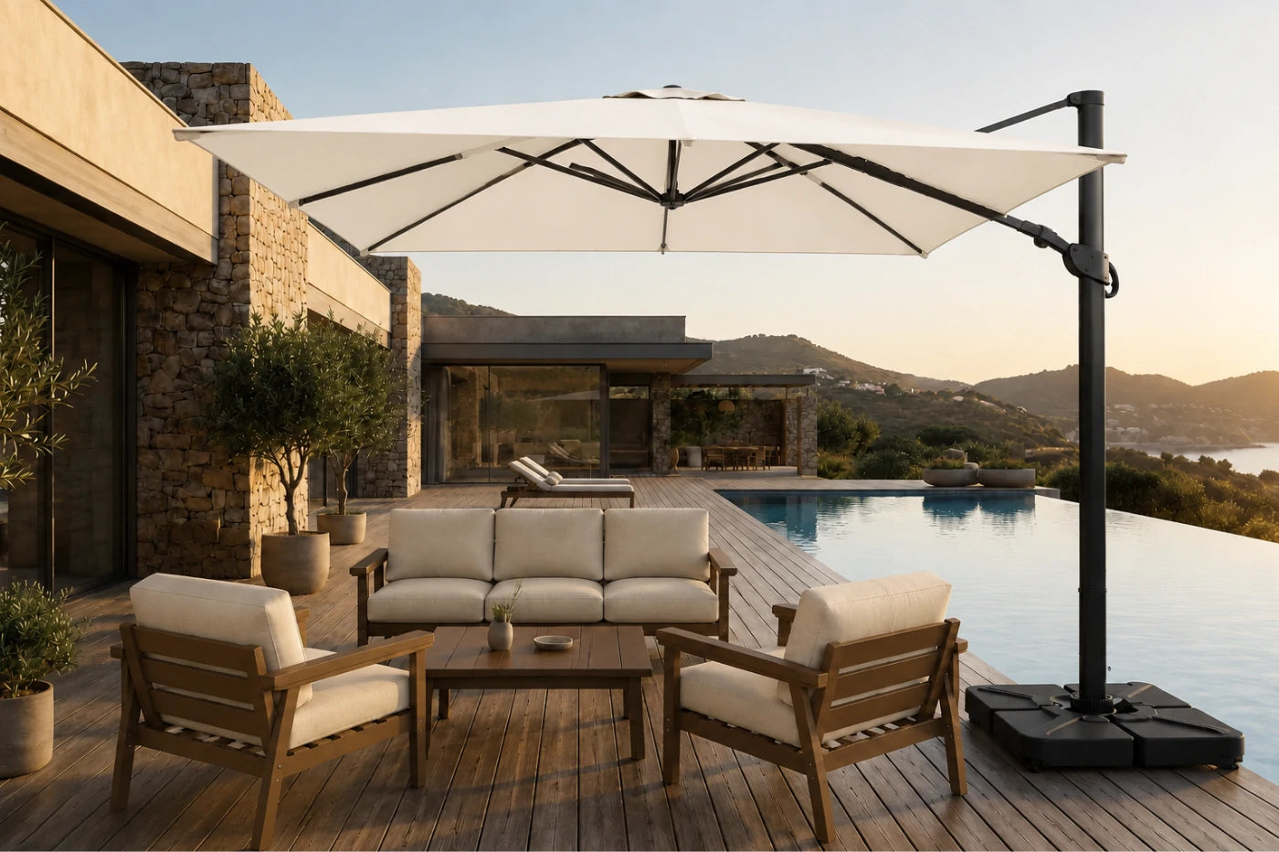 A large creamy white cantilever patio umbrella with a black pole and base, shading a modern outdoor lounge set with wooden chairs and a sofa on a wooden deck beside a swimming pool.