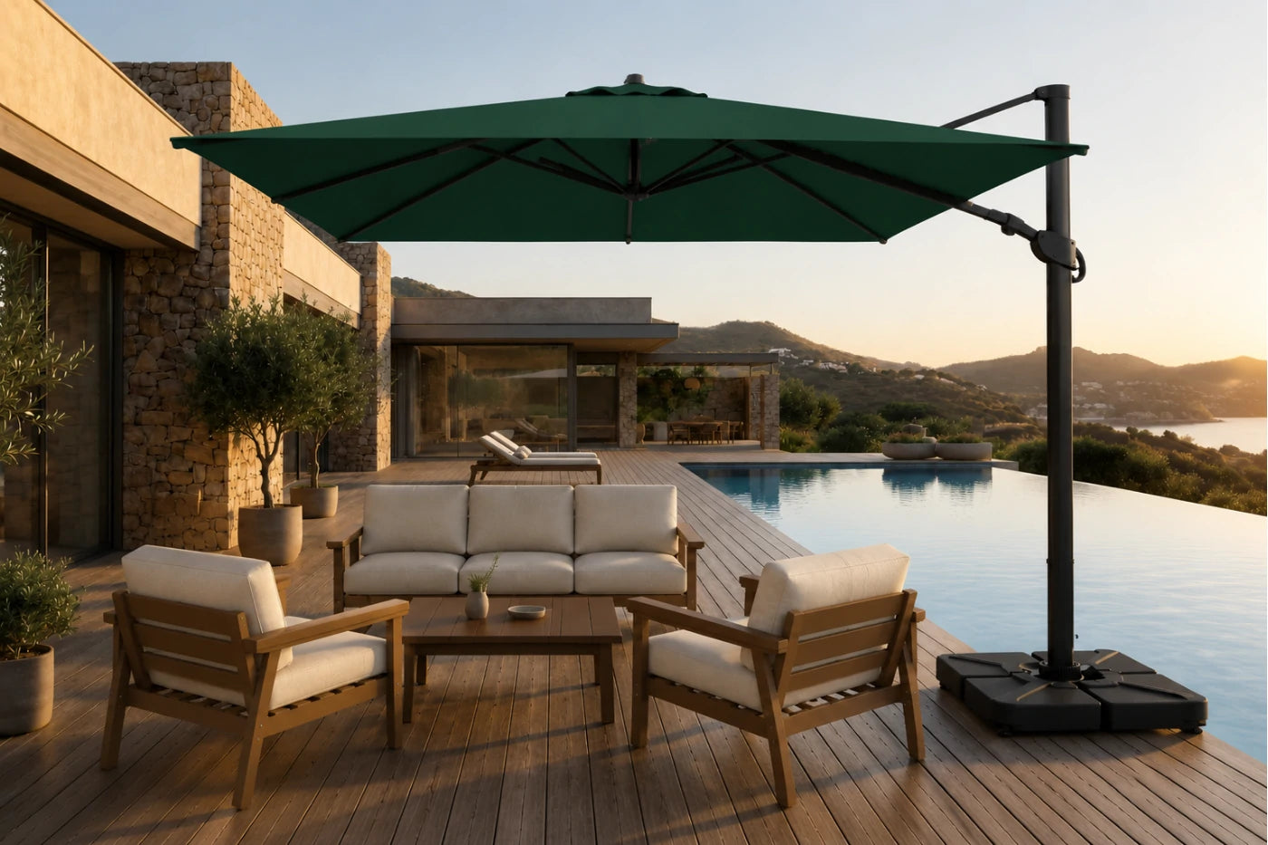 A large dark green cantilever patio umbrella with a black pole and weighted base, shading a wooden outdoor sofa and two matching armchairs on a poolside deck at sunset.