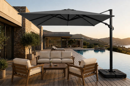 A large dark gray cantilever patio umbrella with a square base is shown outdoors on a wooden deck beside a swimming pool, shading a modern outdoor seating area with wooden chairs and a sofa.