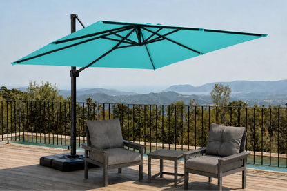 A large teal cantilever patio umbrella with a black pole and base, shown on a wooden deck beside two gray outdoor armchairs and a small side table, with a scenic mountain landscape in the background.
