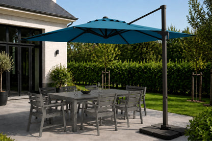 A large lake blue cantilever patio umbrella with a dark metal pole and base, shading a gray outdoor dining table and chairs on a paved patio next to a house.