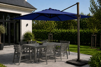 A large navy blue patio umbrella with a cantilever arm and square base, shading a gray outdoor dining table and chairs on a patio next to a house.
